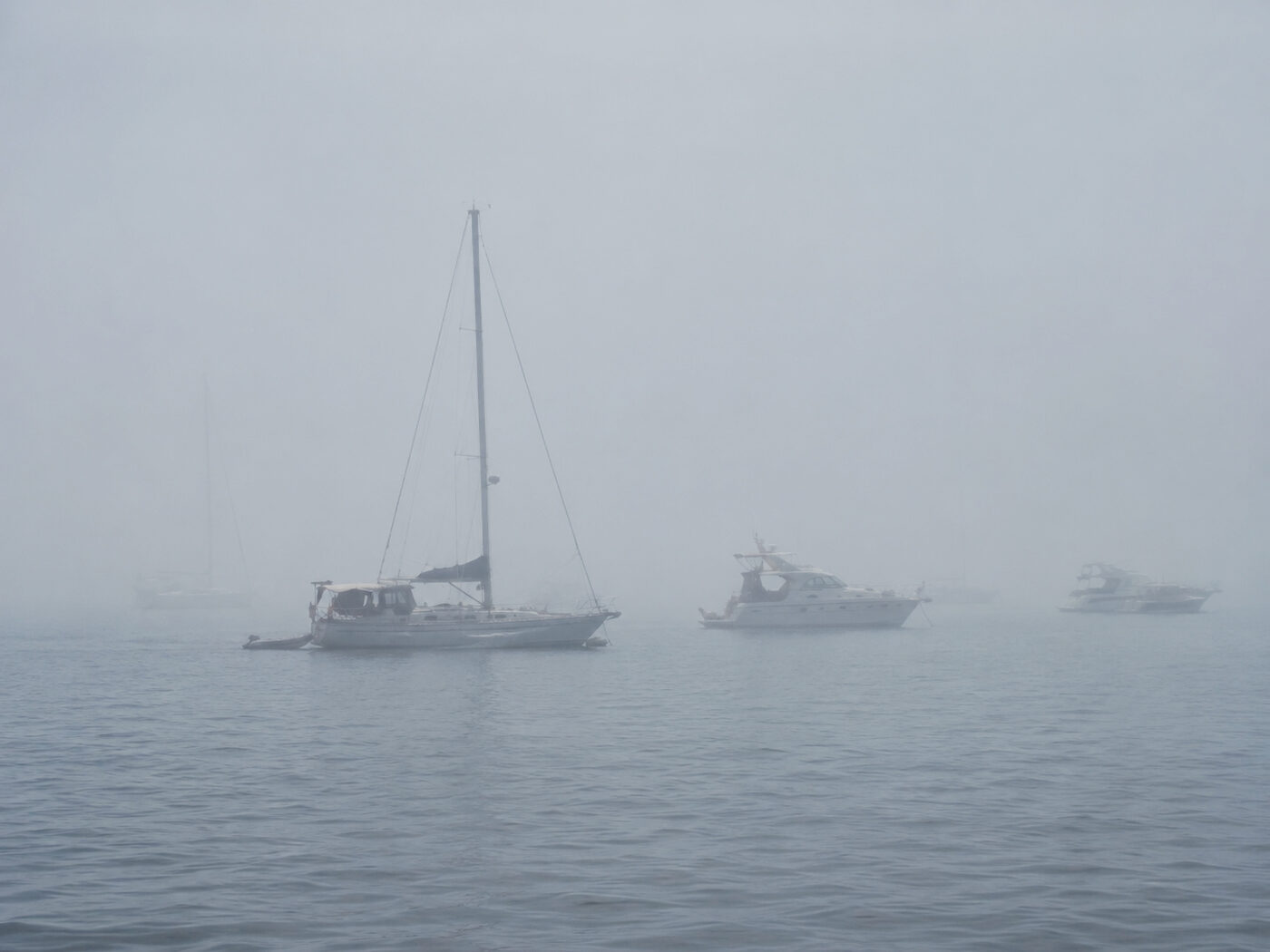 Several boats at anchor barely visible through thick fog